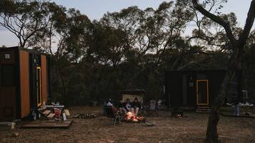 Un camping con una fogata, tiendas de campaña y un pequeño edificio con una puerta.