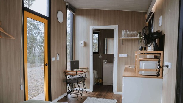 Una habitación compacta y moderna con una cama, una mesita pequeña y un kitchenette.