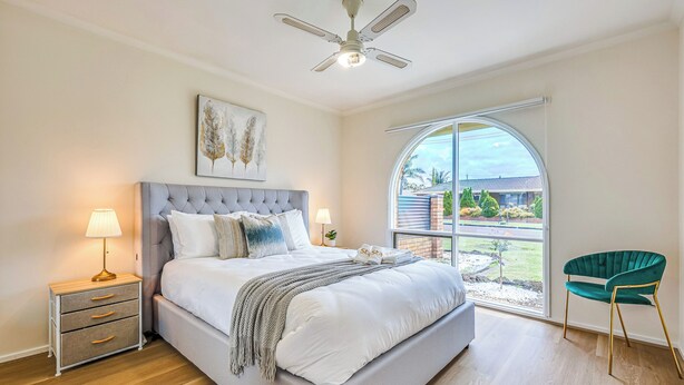 Une chambre avec un grand lit, une table de chevet, une chaise, un ventilateur de plafond et une fenêtre donnant sur l’extérieur.