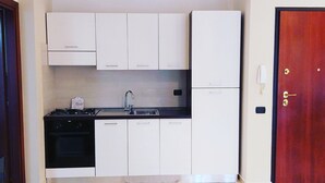 Una cocina compacta con armarios blancos, una estufa negra y una puerta roja.