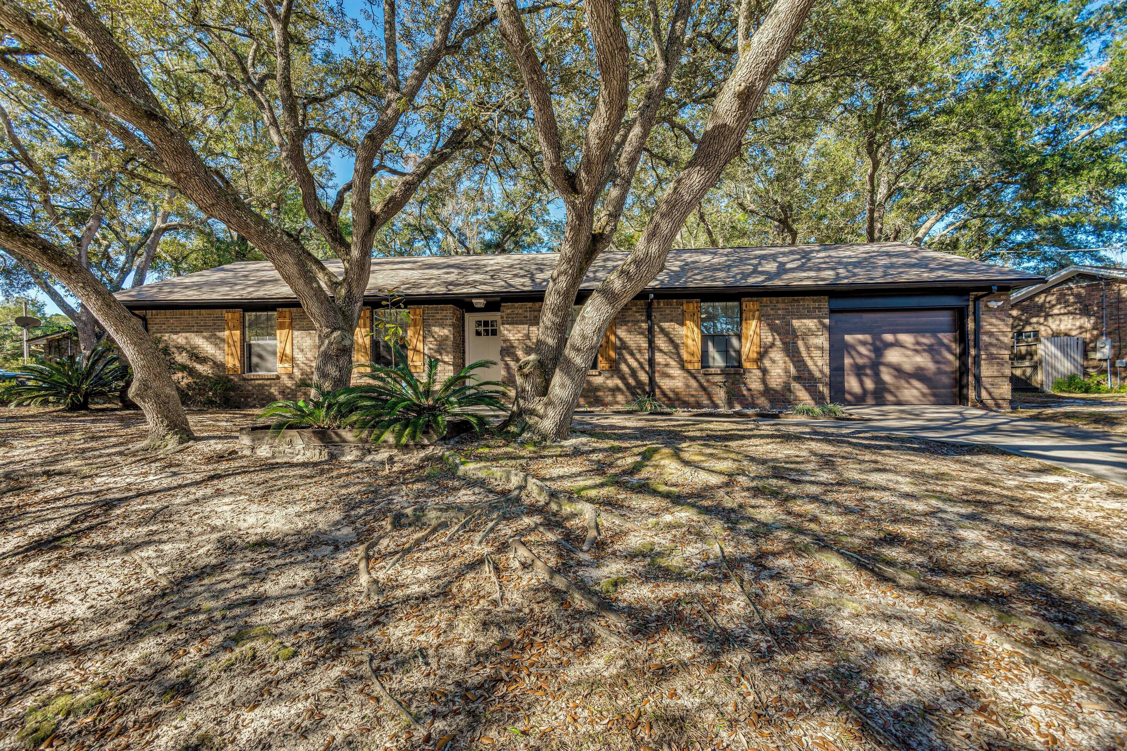 A two-story house with a brick exterior, a garage, and a large tree in front.