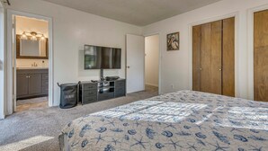 Ein Schlafzimmer mit einem Bett, einem Fernseher, einem Kleiderschrank, einem Spiegel und einem Wäschekorb.
