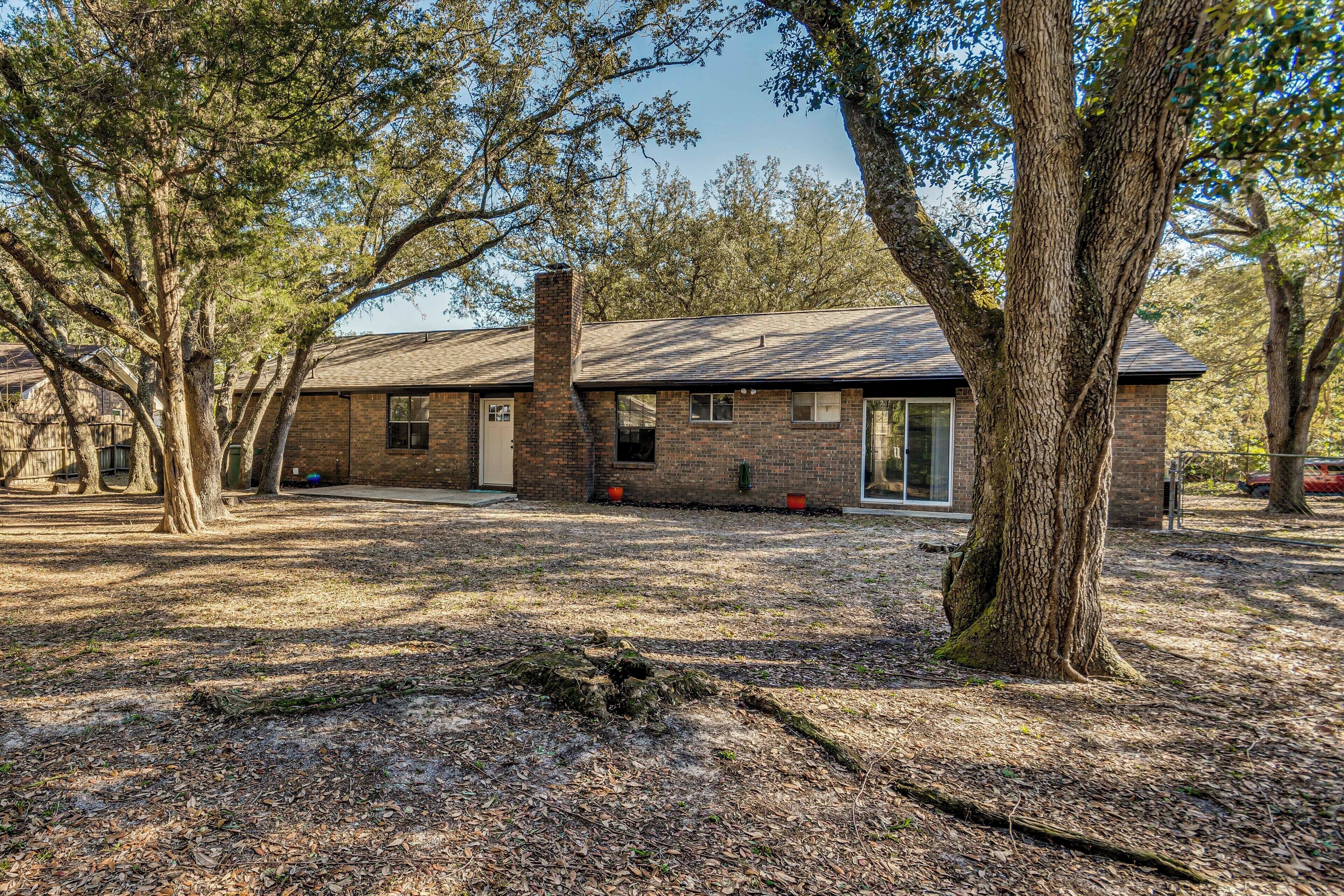 A two-story brick house with a front yard, large trees, and a clear sky.