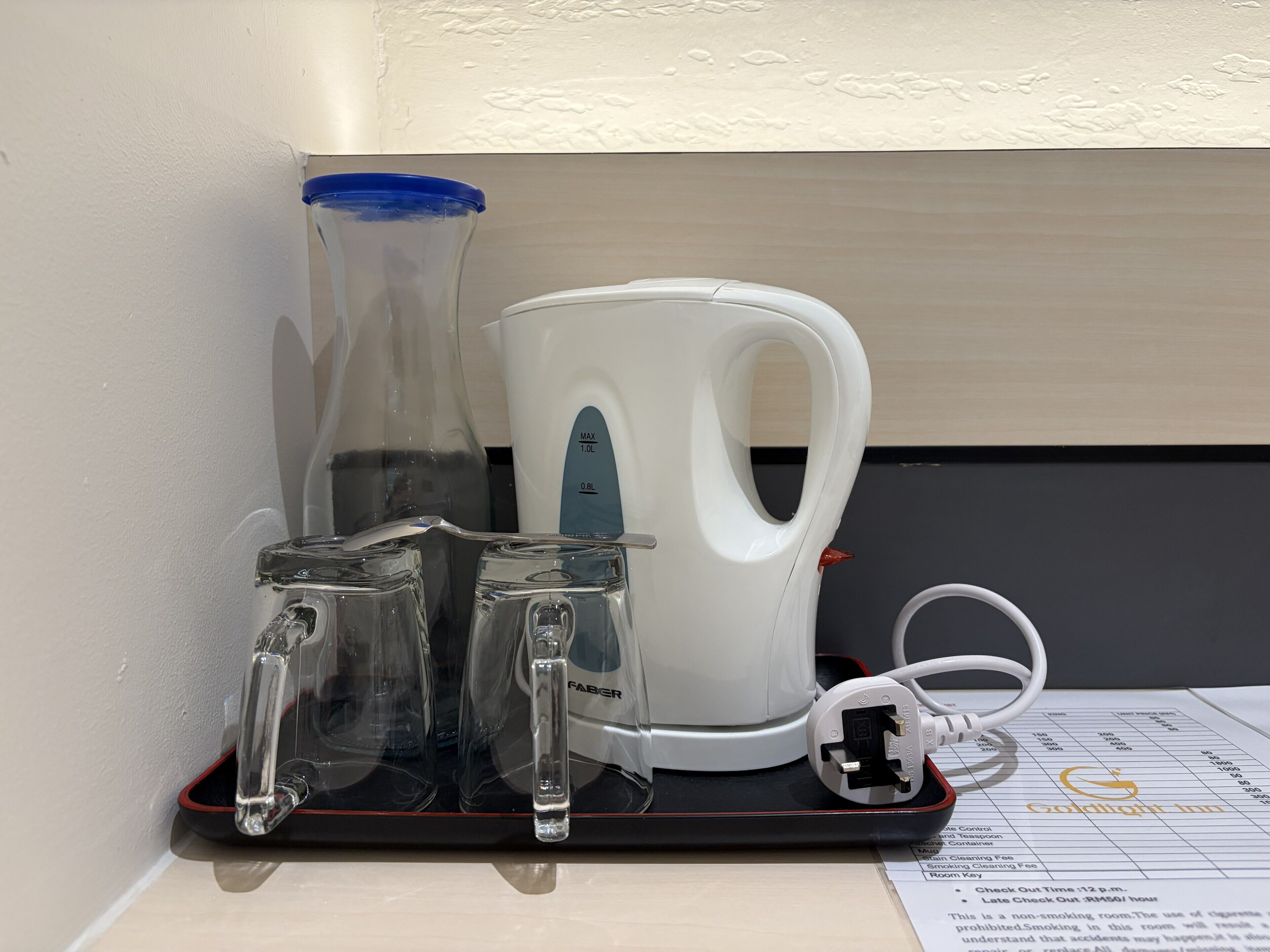 A hotel room with a black charging station, a white kettle, and a glass pitcher.