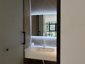 A bathroom with a white sink, a mirror, and a window with a view of the outside.