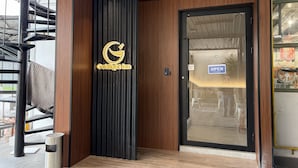 A hotel entrance with a modern design, featuring a logo on the door, a sign indicating the entrance, and a visible trash bin outside.