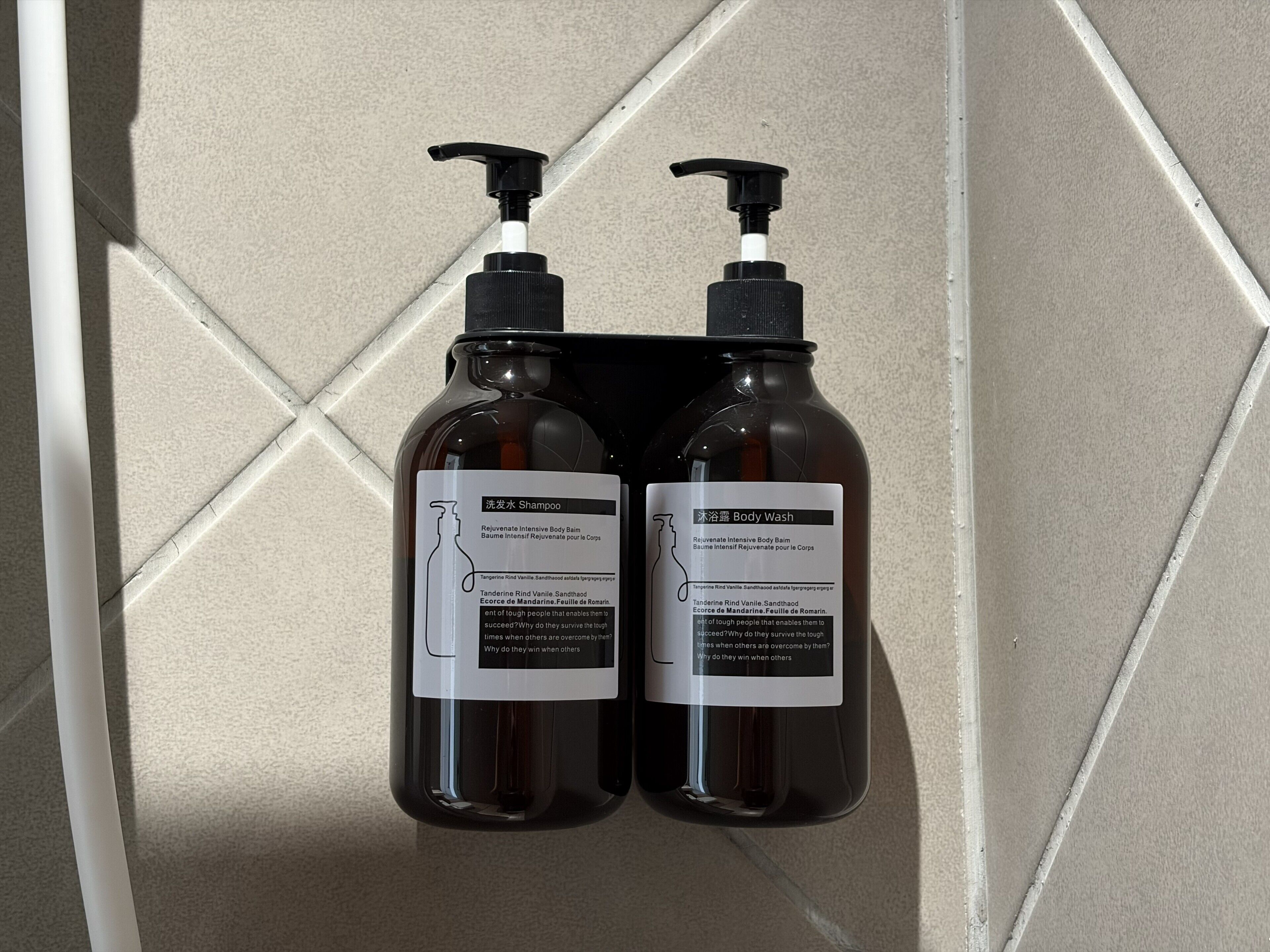 Two bottles of shampoo and body wash on a tiled wall.