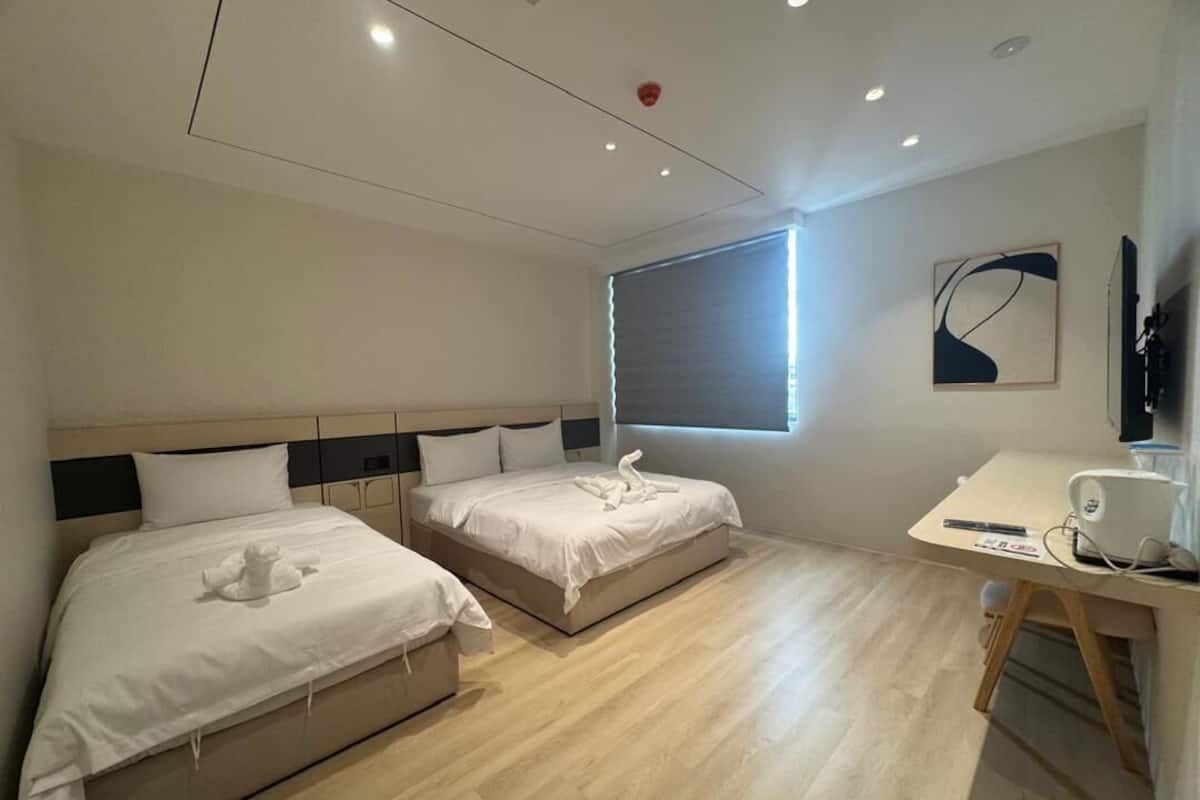 A hotel room with two beds, a desk, and a window.