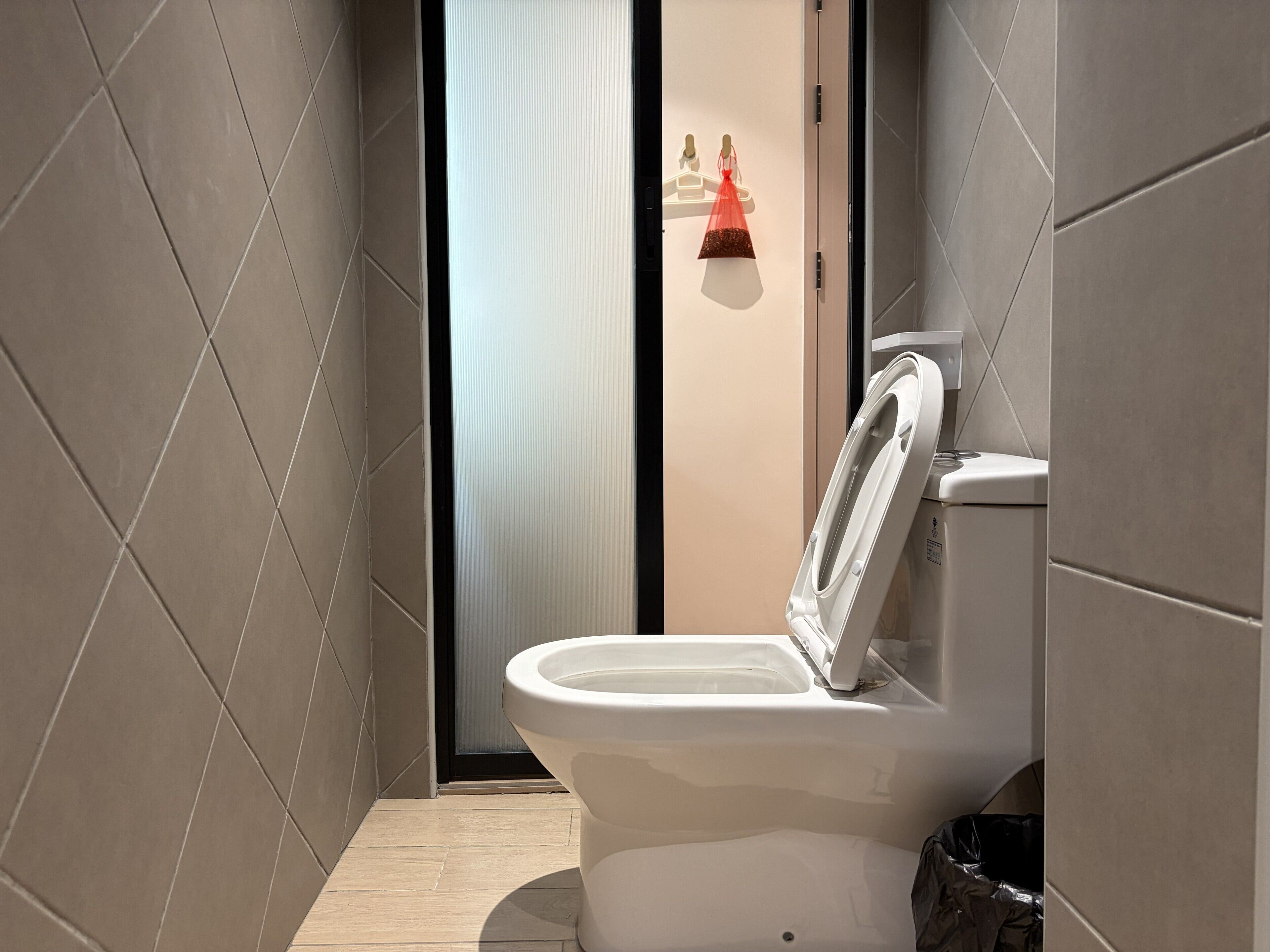 A modern bathroom with a toilet, a trash bin, and a wall-mounted soap dispenser.