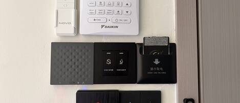 Un termostato, una regleta de enchufes, un lector de tarjetas y un cargador portátil de batería en una pared.