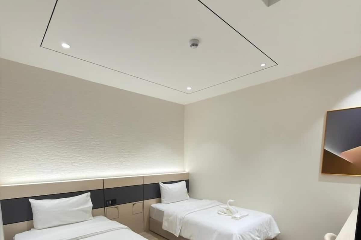 A modern hotel room with two beds, a wooden floor, and a ceiling light fixture.