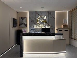 A reception desk with a marble wall backdrop, a digital display, and a sign reading "Goldlight Inn."