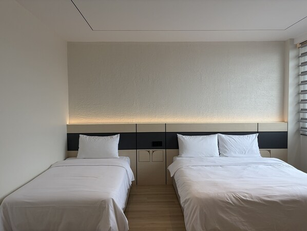 Quarto de hotel com duas camas de solteiro, piso de madeira, parede texturizada e cabeceira com iluminação embutida.