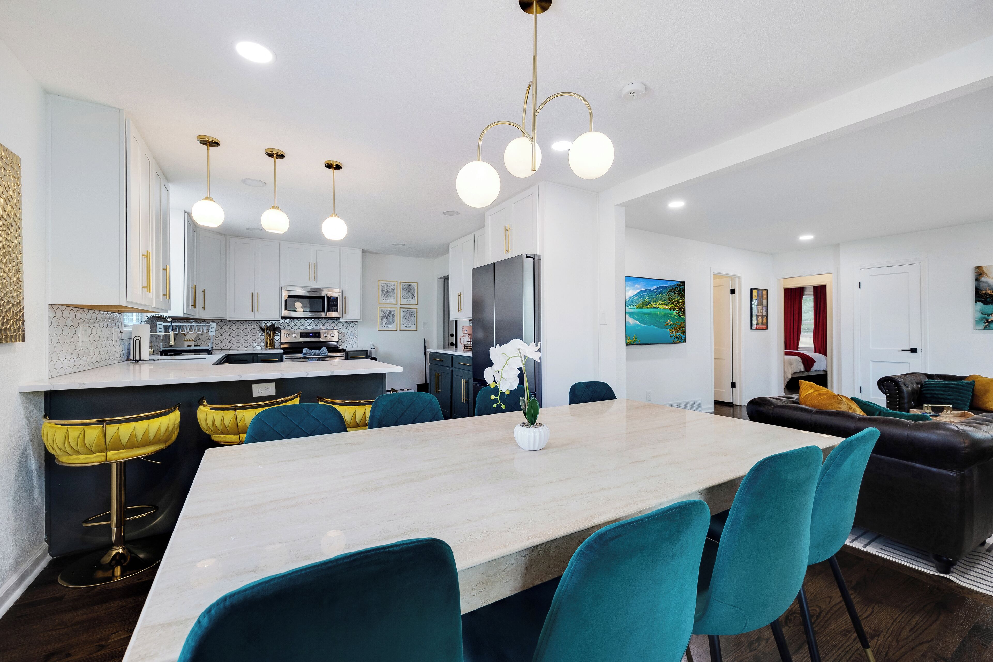 Una cucina moderna con mobili bianchi, un'isola centrale con sgabelli da bar e un'area pranzo con sedie color acquamarina.