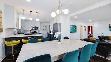 Una cucina moderna con mobili bianchi, un'isola centrale con sgabelli da bar e un'area pranzo con sedie color acquamarina.