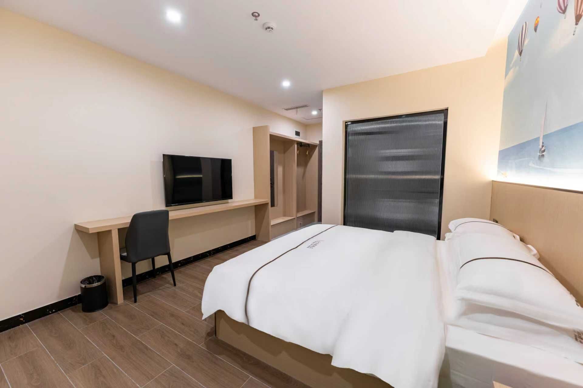 A hotel room with a bed, a desk with a TV, a wardrobe, and a window with blinds.
