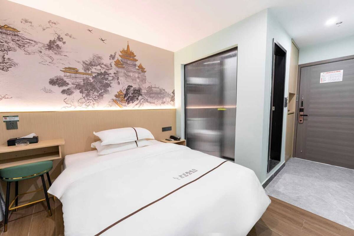 Ein Hotelzimmer mit einem Bett, einem Schreibtisch, einem Stuhl, einer Wand mit Wandgemälde, einer Tür und einem kleinen Tisch.