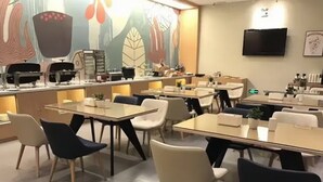 A modern dining area with tables and chairs, a kitchen area, and a flat-screen TV on the wall. - Aura Crane Hotel Shenzhen Nanshan Xili Metro Station Branch (Shenzhen)