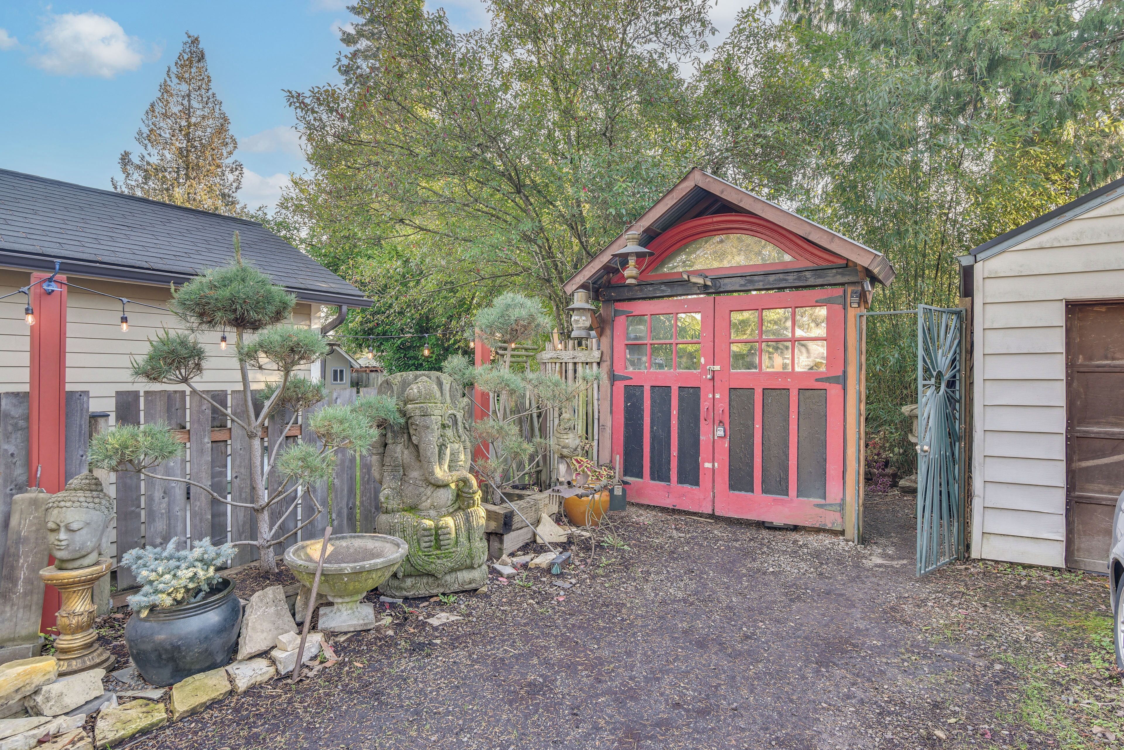 A garden with a red gate, potted plants, and a Buddha statue.