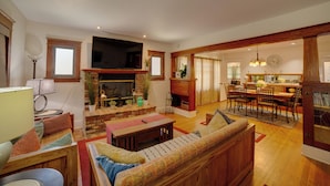 A living room with a fireplace, a television, a dining area with chairs and a table, and a kitchen in the background. - Home 1/2 Mi to Dtwn Riverside: Families Welcome! (Riverside)