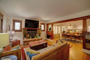 A living room with a fireplace, a television, a dining area with chairs and a table, and a kitchen in the background. - Home 1/2 Mi to Dtwn Riverside: Families Welcome! (Riverside)