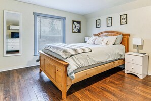 Une chambre à coucher avec un lit en bois, une table de chevet, une commode et une fenêtre avec des stores.