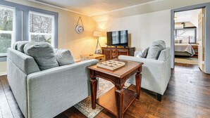 Un salon avec deux canapés gris, une table basse en bois, un téléviseur et une lampe.