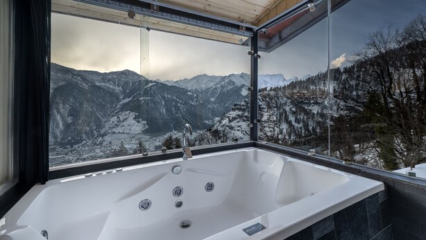 A modern bathroom with a large bathtub, a window offering a mountain view, and a wooden ceiling. - Echor Himalayan Sky Cabins Sethan Manali (Manali)