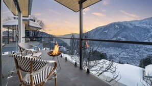 A modern balcony with wicker chairs and a fire table, overlooking a snowy mountain landscape. - Echor Himalayan Sky Cabins Sethan Manali (Manali)