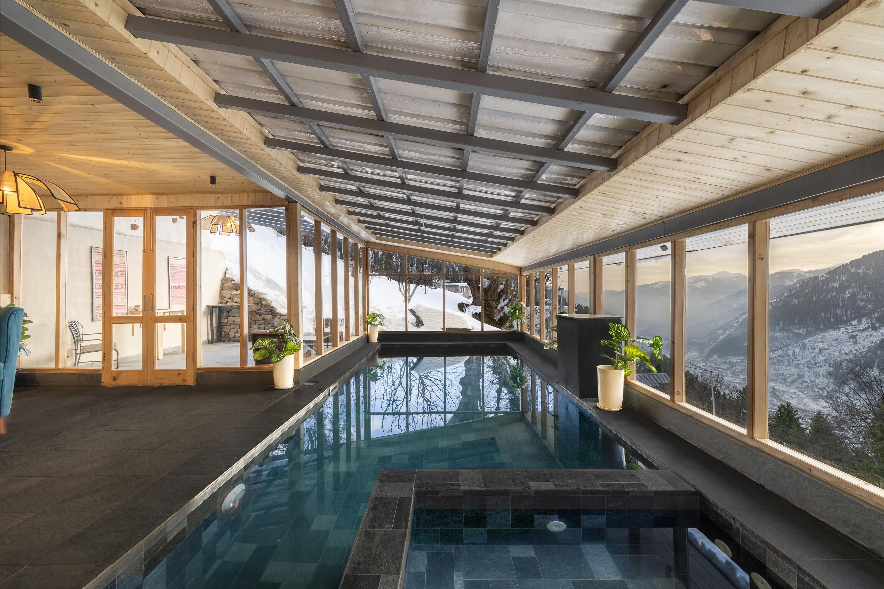 An indoor swimming pool with a view of a snowy mountain landscape through large windows.