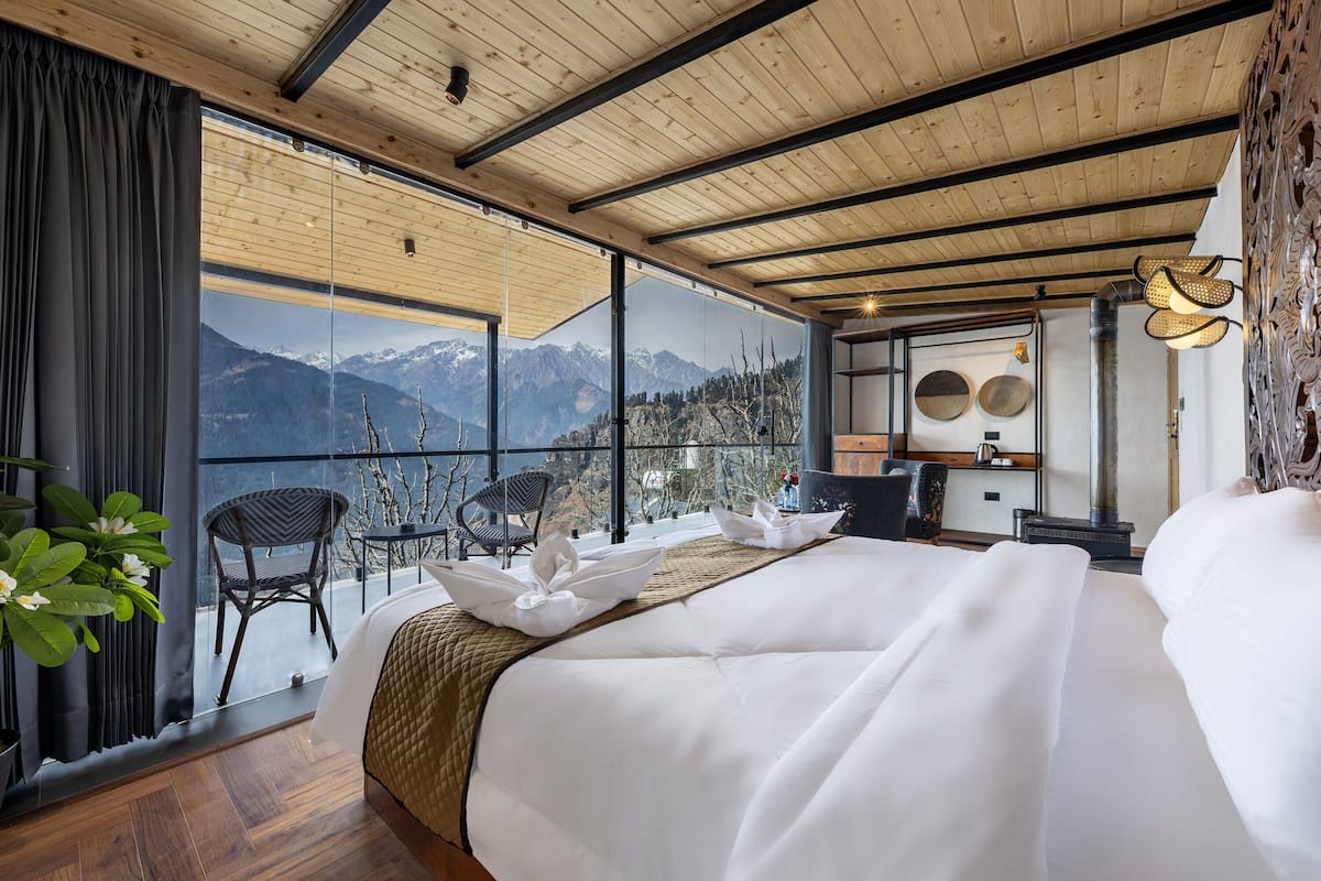 A bedroom with a large bed, a view of mountains, and a balcony with chairs.