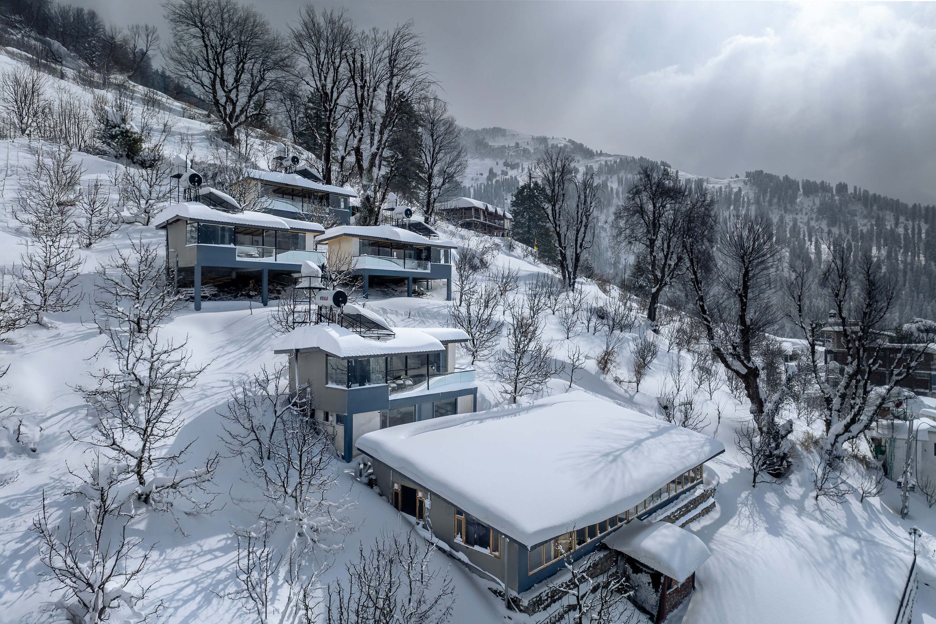 A modern ski resort with multiple buildings, snow-covered roofs, and a mountainous backdrop.
