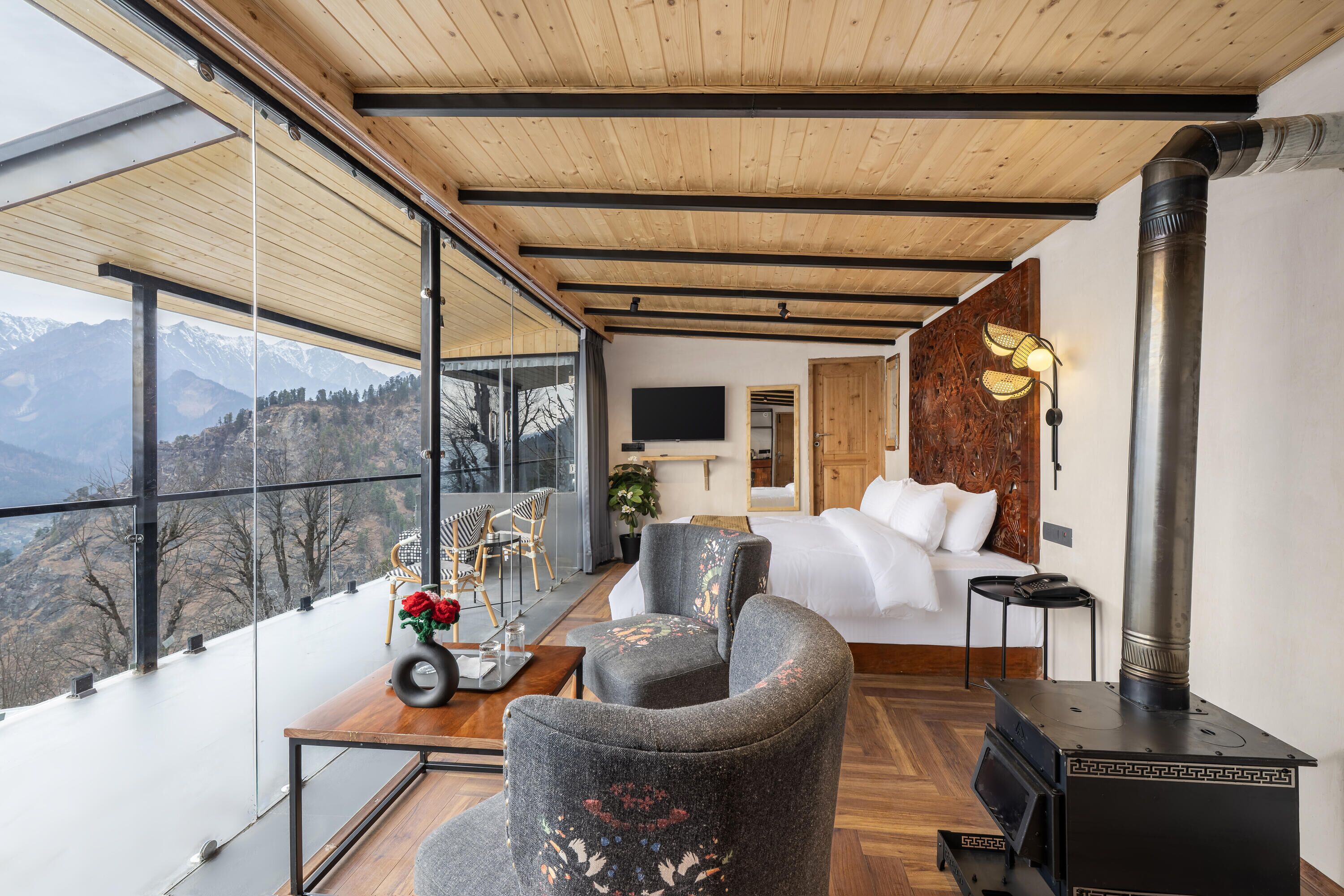 A modern room with a large window, a bed, a sofa, and a wood-burning stove.
