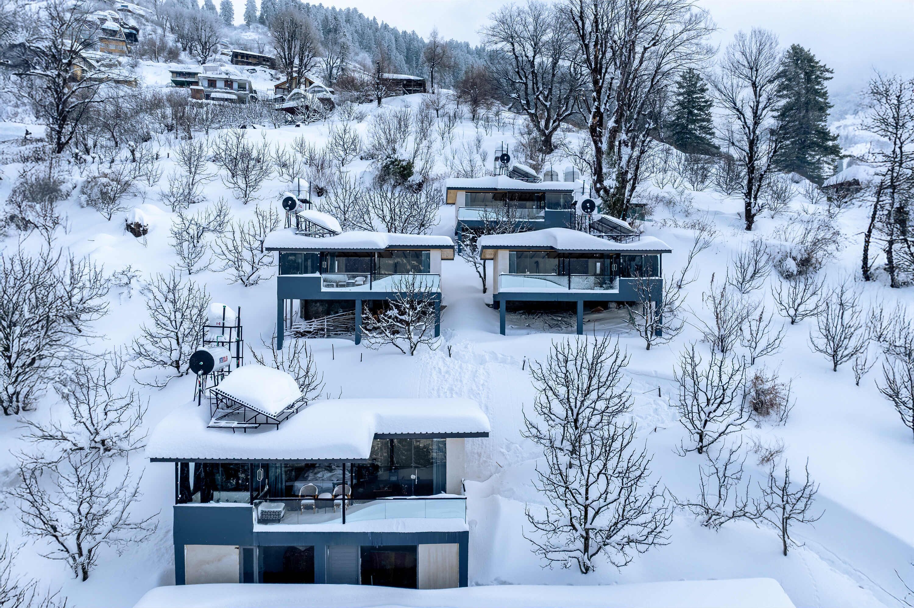 Un edificio moderno de varios pisos con grandes ventanales y techo plano, rodeado de árboles nevados y un paisaje montañoso.
