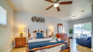 A bedroom with a wooden bed, two bedside tables with lamps, a ceiling fan, a large mirror, and a view of the outdoors through a sliding glass door. - Family-Friendly Home 2 Mi to Dtwn Riverside (Riverside)