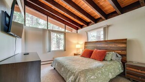 Una camera da letto con soffitto in legno, un letto con biancheria da letto floreale, un comodino, una lampada e un televisore su un mobile.