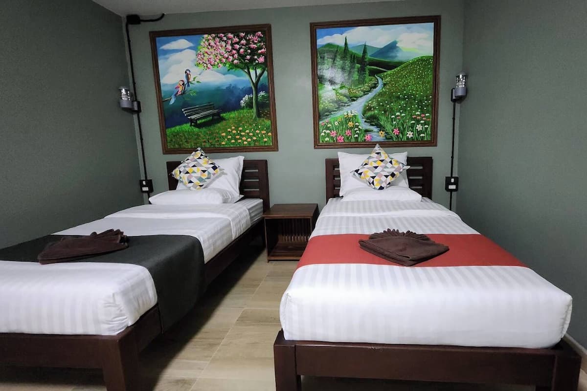 Ein Hotelzimmer mit zwei Einzelbetten, einem roten Bettüberwurf und zwei Bildern an der Wand.