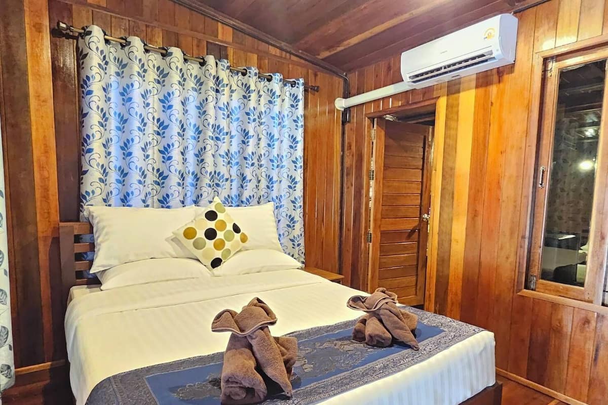 Ein Zimmer mit Holzwandverkleidung, einem Bett, einem Fenster und einer Klimaanlage.