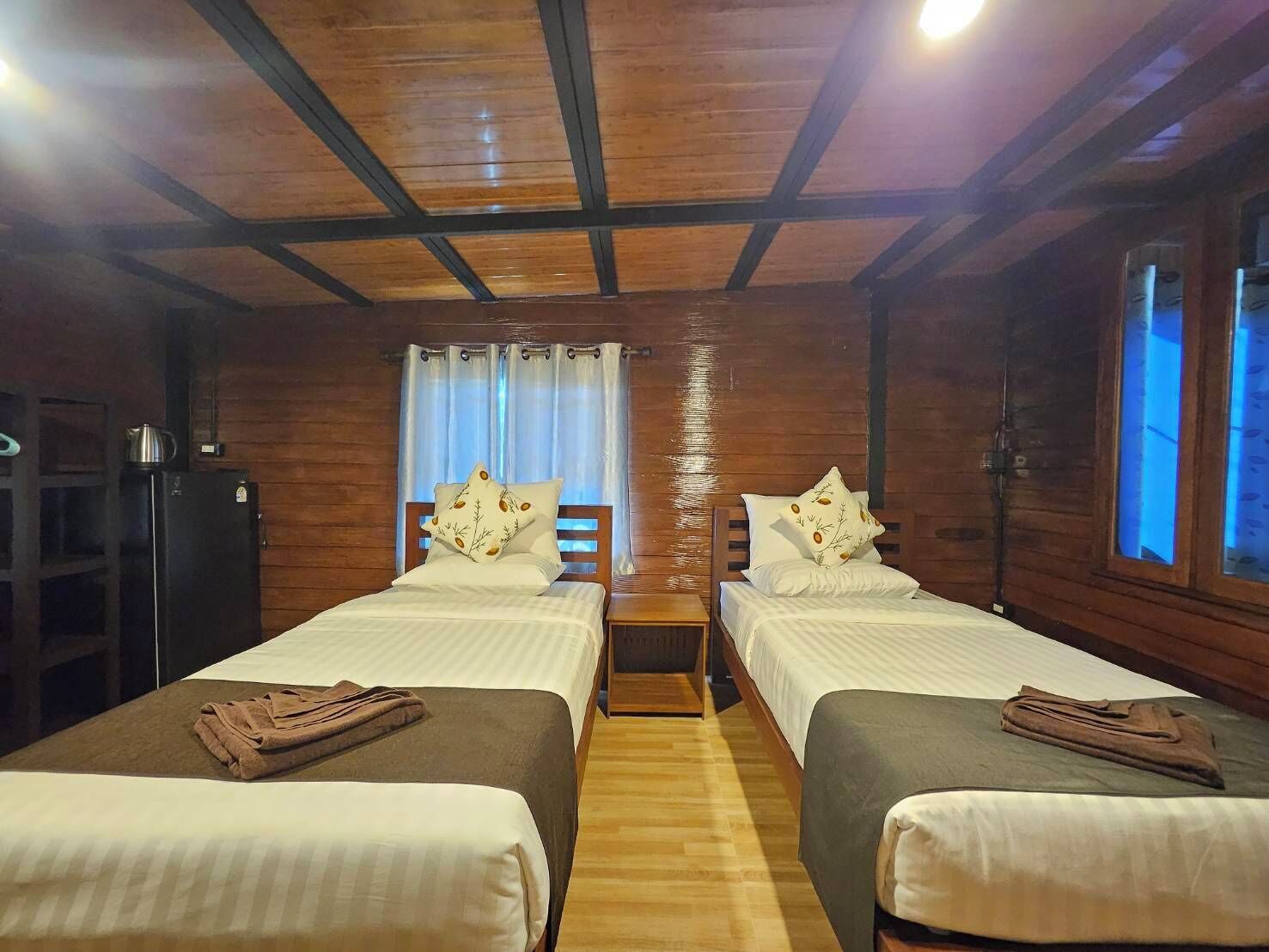 Une chambre avec deux lits, des murs en bois, un plafond en bois, une petite table et une fenêtre avec des rideaux.