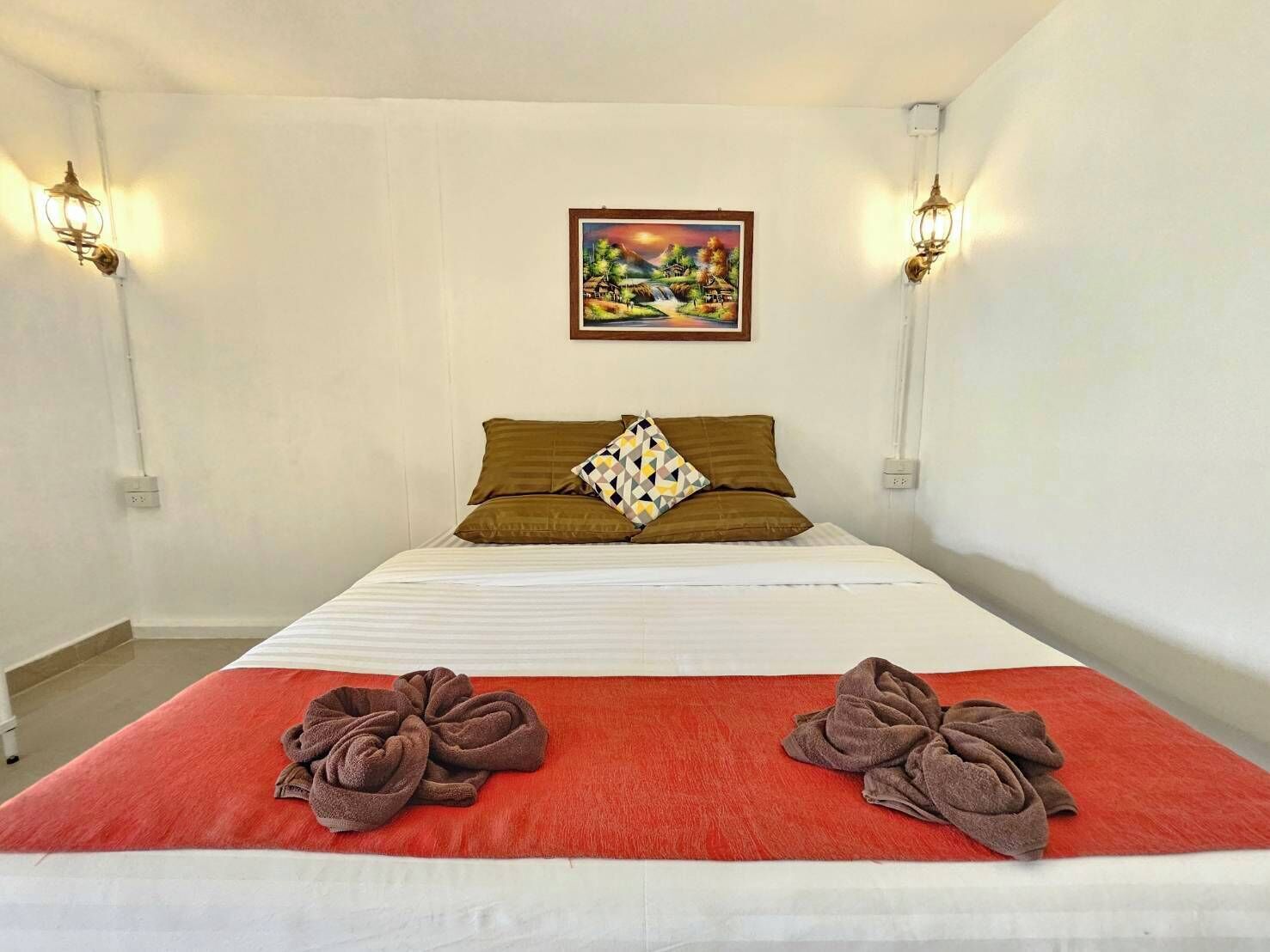 Ein Hotelzimmer mit einem Bett, zwei Wandleuchten, einem Gemälde über dem Bett und zwei Handtüchern auf dem Bett.