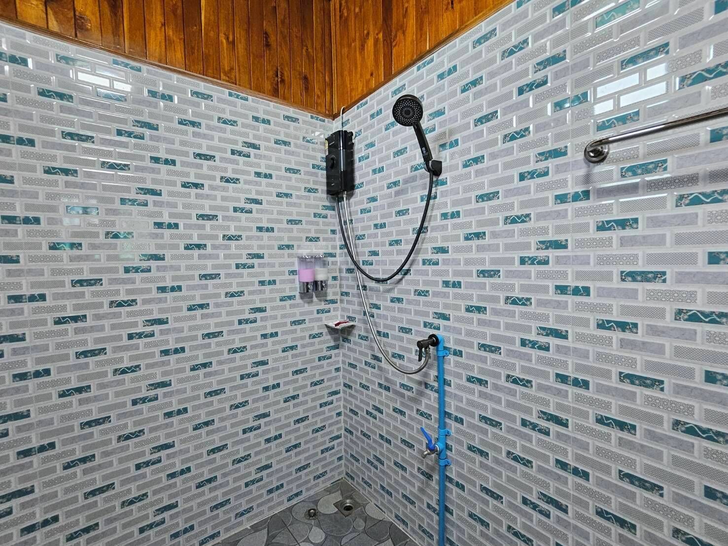 A shower area with a tiled wall, a wooden ceiling, and a handheld showerhead.