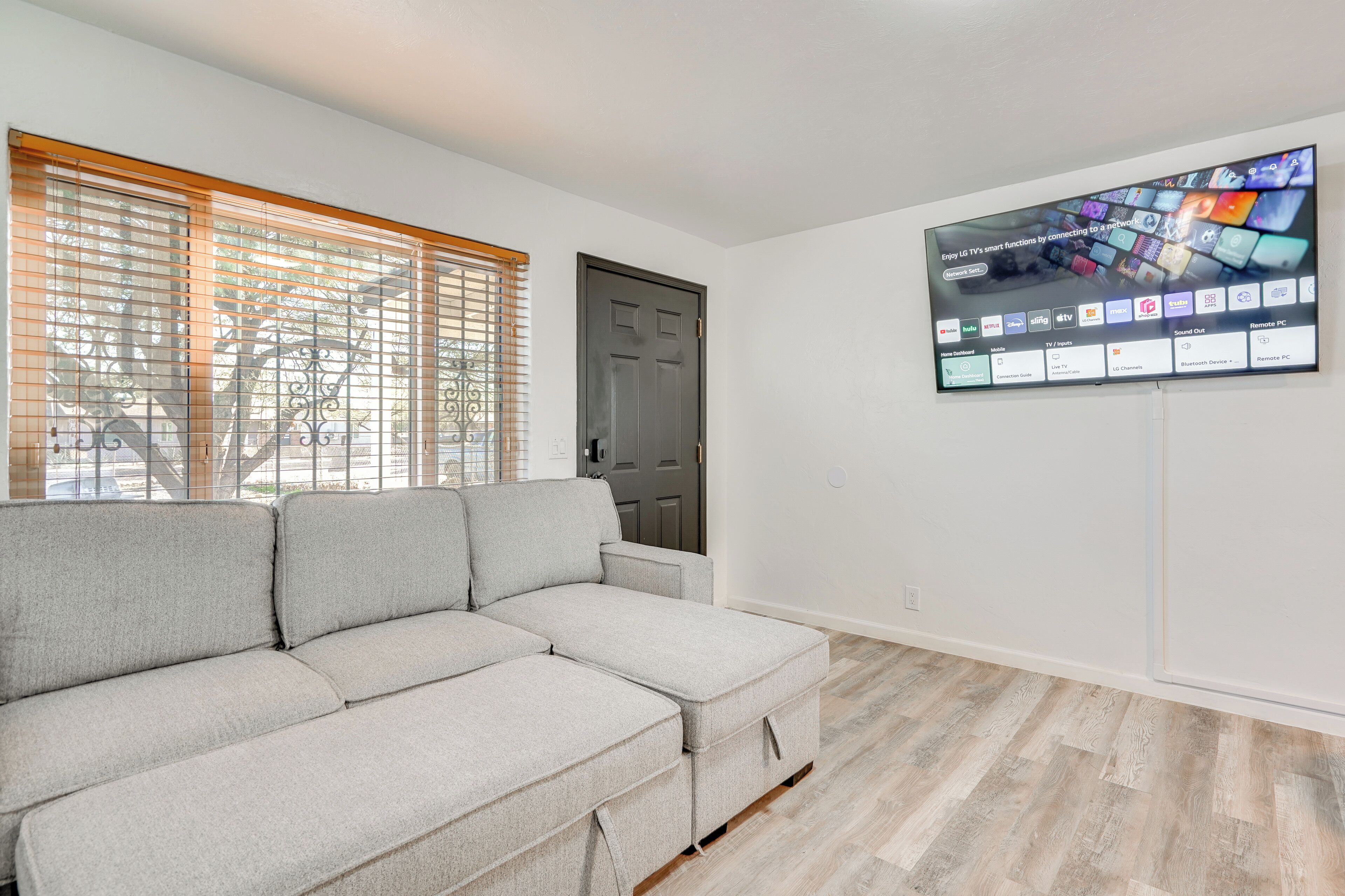 Een woonkamer met een hoekbank, een flatscreen televisie aan de wand en een deur.
