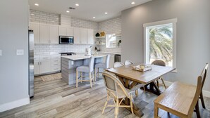 A modern kitchen with white cabinets, a wooden dining table, and a large window. - Easy Beach Access! Port A Oasis w/ Private Pool (Port Aransas)