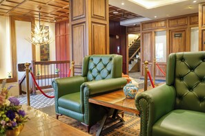 Un hall con sillones tapizados en verde, una mesa de madera, una araña y una escalera.