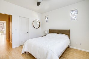 Un dormitorio con cama de madera, paredes blancas, un espejo redondo y un pequeño ventanal con vidrieras.