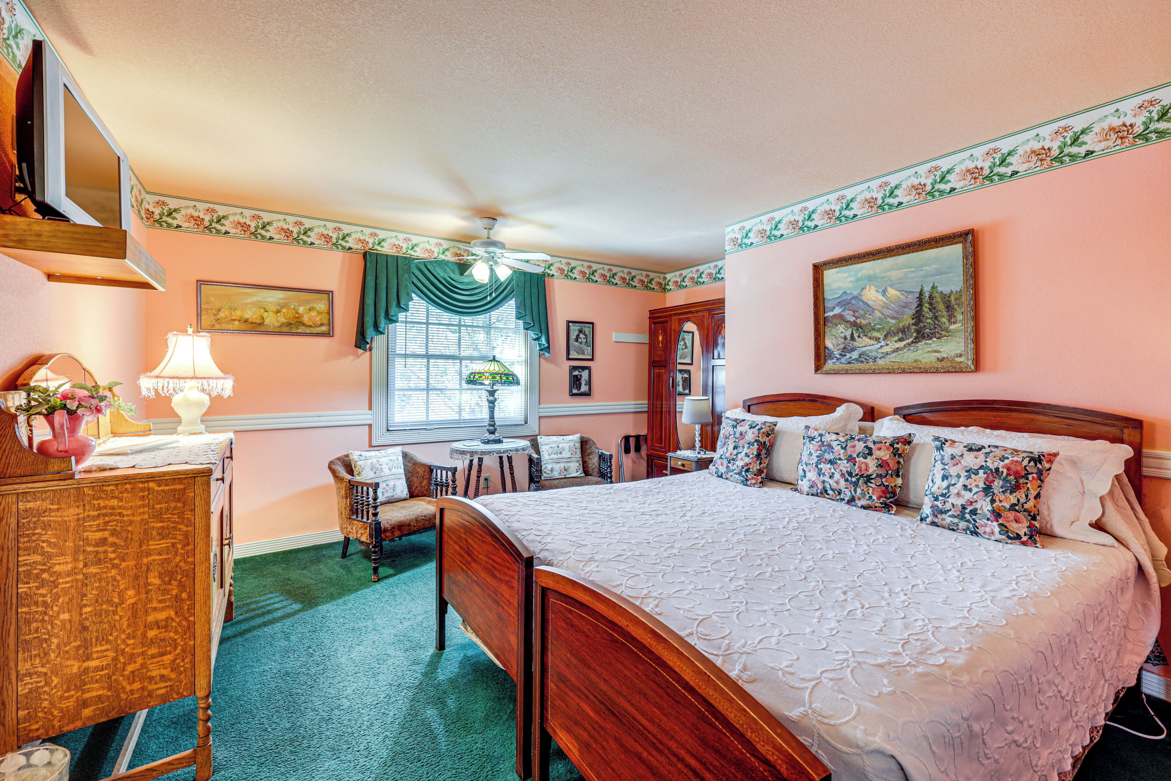 A bedroom with a wooden bed, a desk, a chair, and a window with curtains.