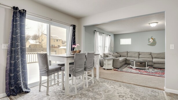 A living room with a dining area, a gray sofa, a patterned rug, and a view of the outside. - Spacious Family Getaway w/ Yard in Kalamazoo! (Kalamazoo)