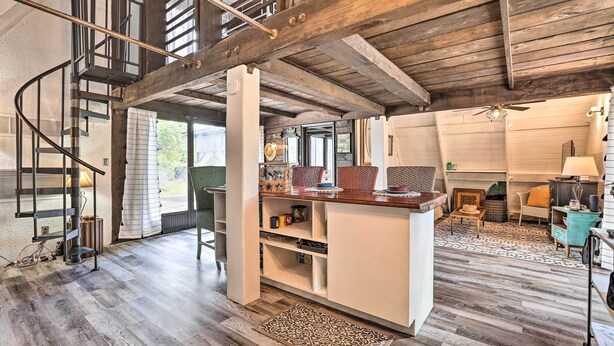 Un interior espacioso con una escalera de madera, una isla central con estantes y una zona de estar acogedora con chimenea.