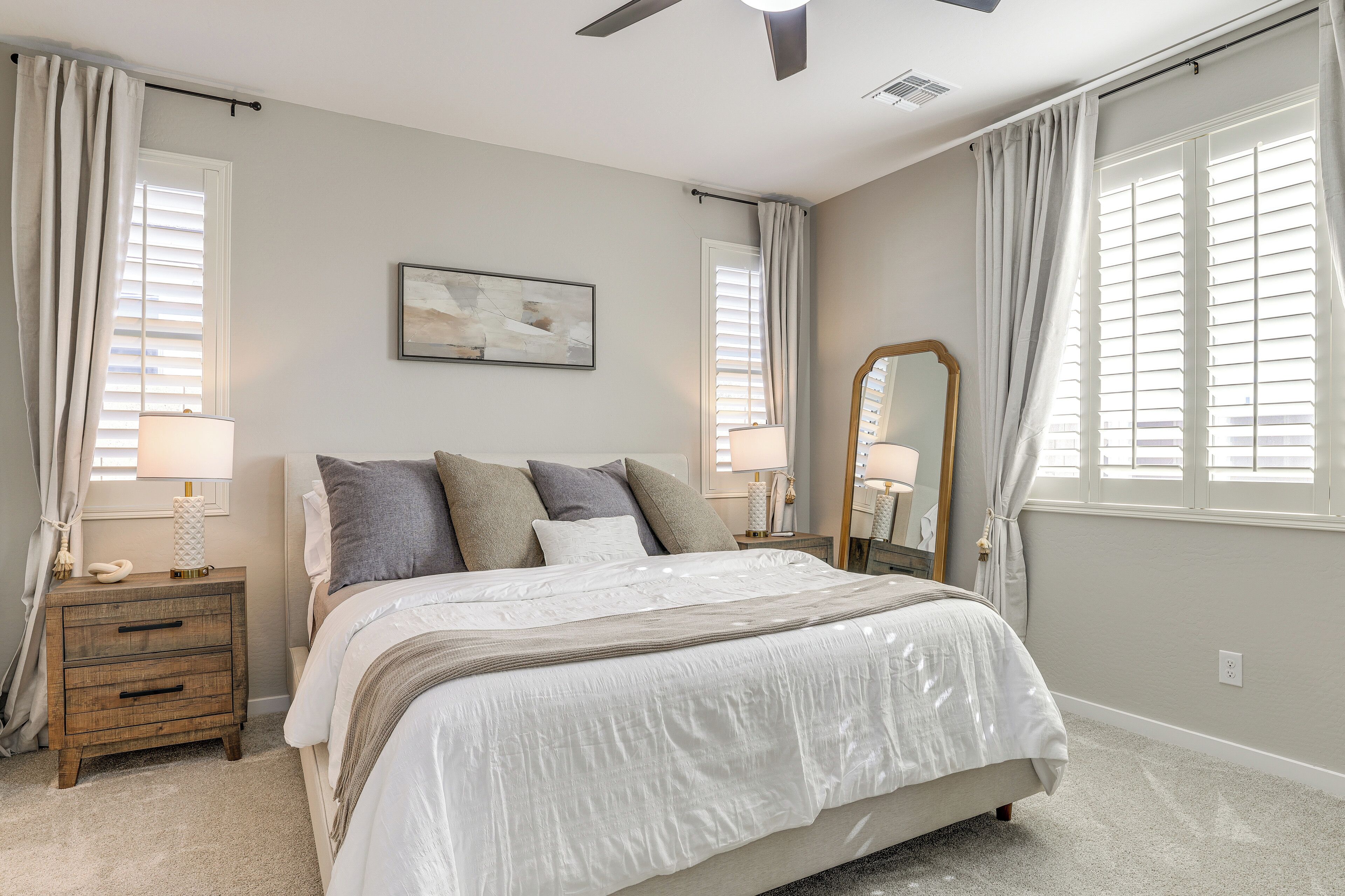 A bedroom with a bed, nightstands, a mirror, and a ceiling fan.