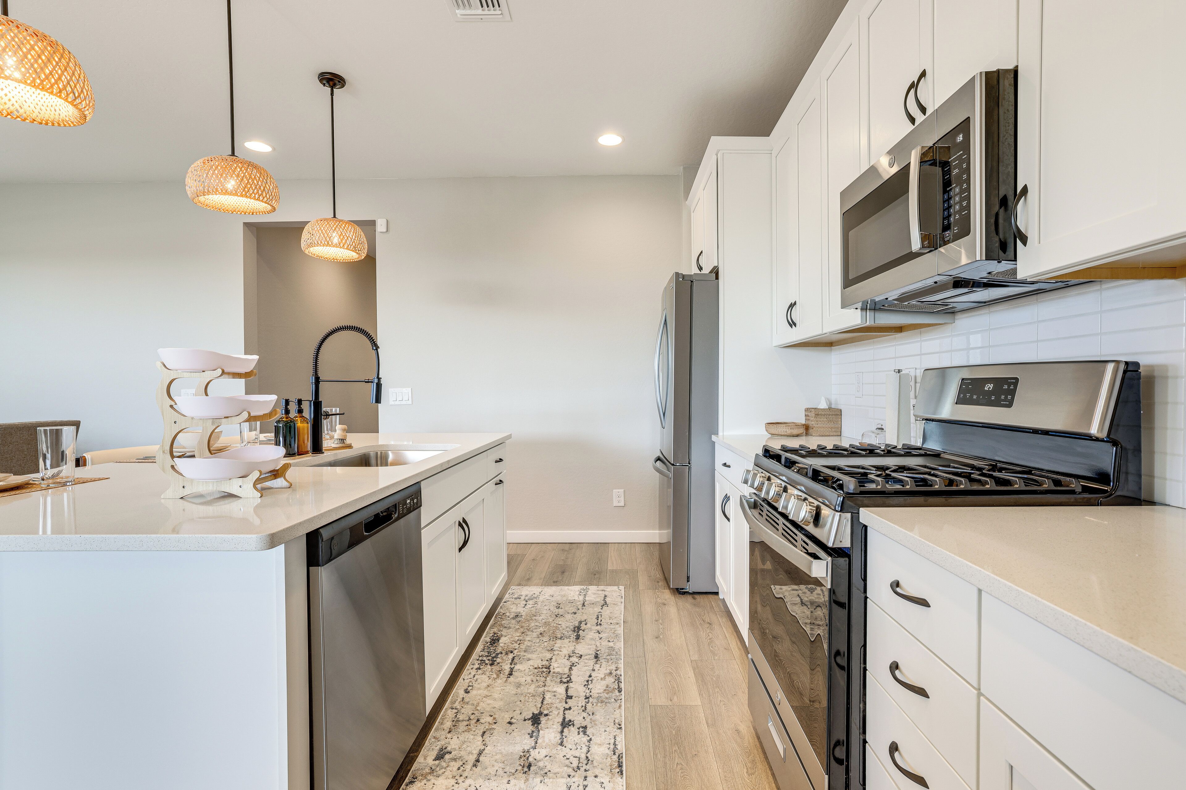 A modern kitchen with white cabinetry, stainless steel appliances, and pendant lighting.